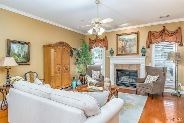 living area featuring a ceiling fan, visible vents, crown molding, a fireplace with flush hearth, and light wood-style floors
