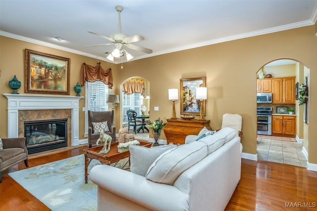 living room featuring arched walkways, ceiling fan, ornamental molding, and light wood finished floors