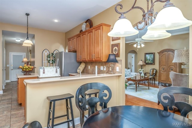 kitchen with a ceiling fan, backsplash, light countertops, freestanding refrigerator, and a peninsula