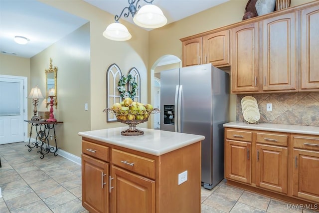 kitchen with a kitchen island, light countertops, stainless steel fridge with ice dispenser, arched walkways, and backsplash