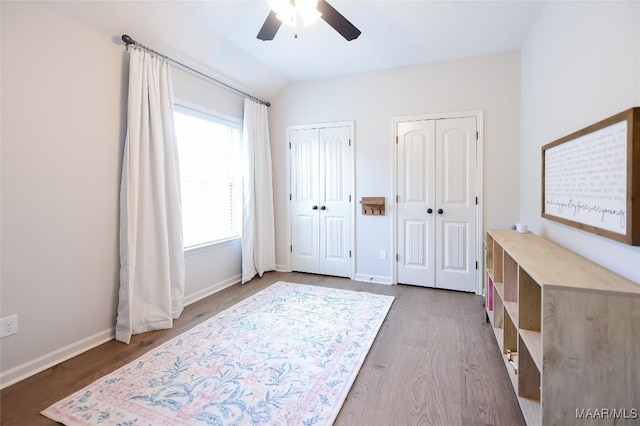 unfurnished bedroom with baseboards, a ceiling fan, multiple closets, and wood finished floors