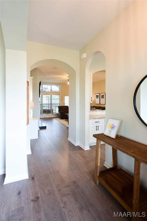 hallway with baseboards, arched walkways, and dark wood-style flooring