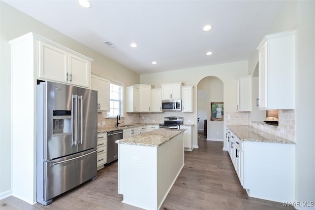 kitchen with a kitchen island, backsplash, stainless steel appliances, and white cabinets