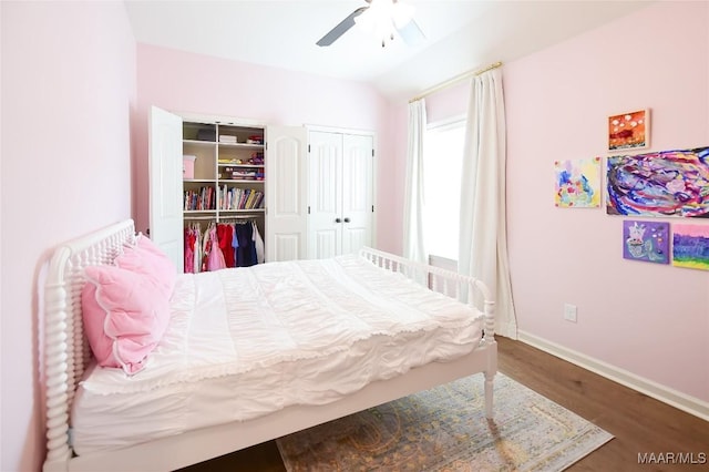 bedroom with multiple closets, a ceiling fan, baseboards, wood finished floors, and vaulted ceiling