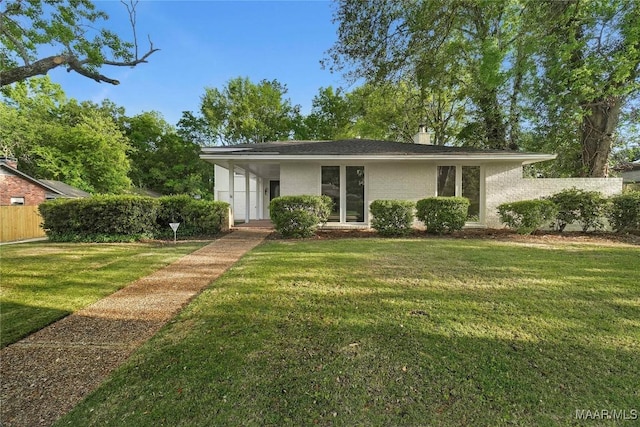 view of front of property featuring brick siding, fence, a chimney, and a front lawn