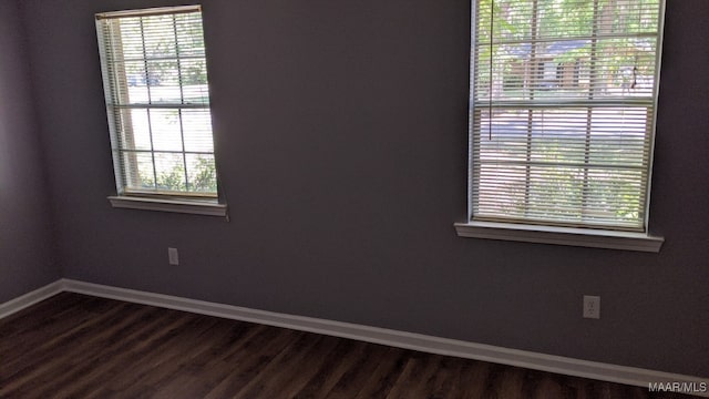 empty room featuring baseboards, a healthy amount of sunlight, and dark wood-style floors