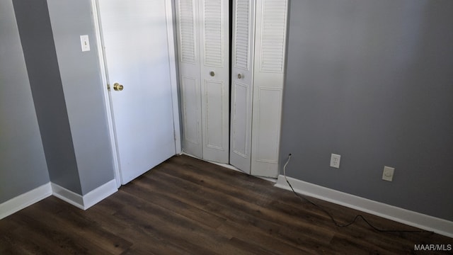 unfurnished bedroom featuring dark wood-style flooring, baseboards, and a closet