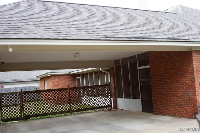 exterior space with roof with shingles, fence, a sunroom, and brick siding