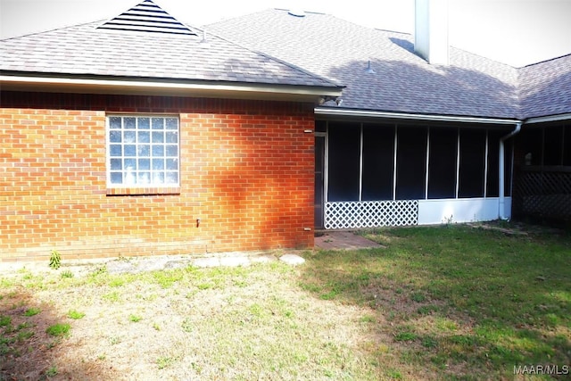 view of property exterior featuring a yard, brick siding, a shingled roof, and a sunroom