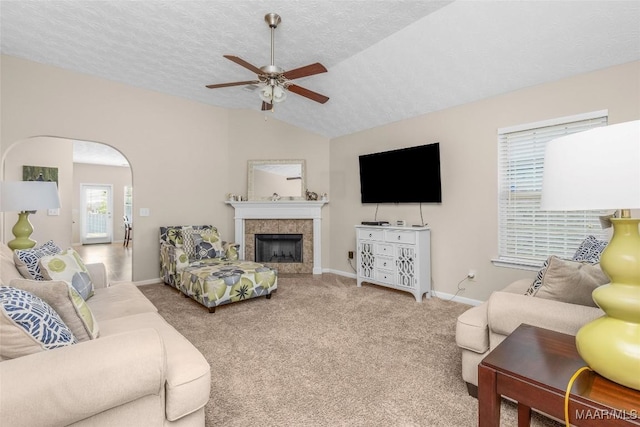 carpeted living room with ceiling fan, a textured ceiling, baseboards, lofted ceiling, and a tile fireplace