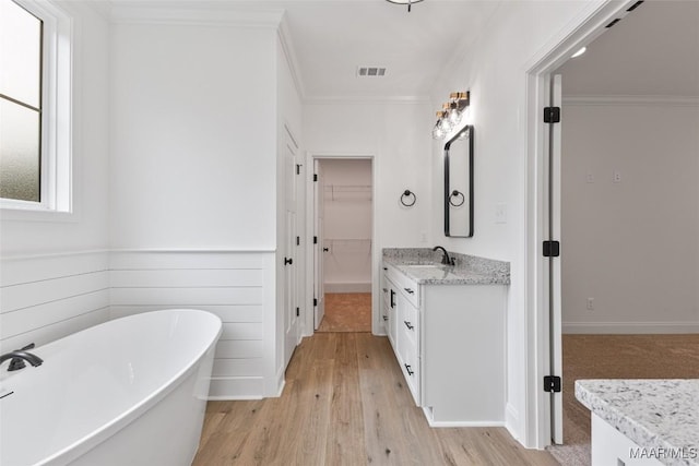 full bathroom with vanity, a freestanding tub, wood finished floors, visible vents, and ornamental molding