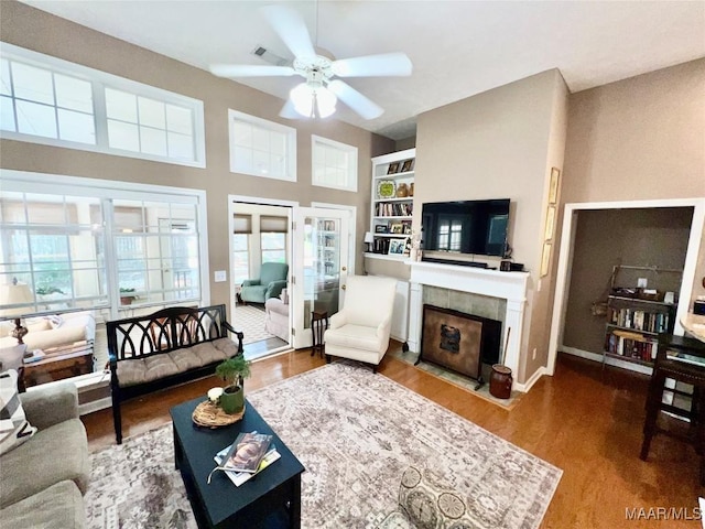 living area with wood finished floors, a fireplace, baseboards, ceiling fan, and built in shelves