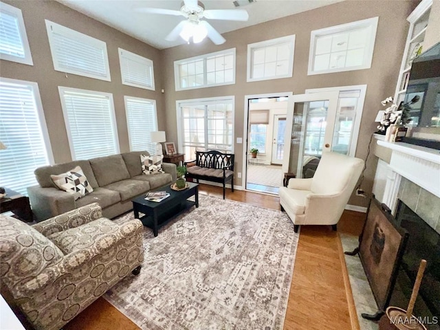 living room with a towering ceiling, ceiling fan, a tile fireplace, and light wood-type flooring