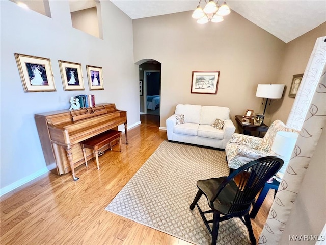 living area with arched walkways, baseboards, light wood finished floors, and high vaulted ceiling