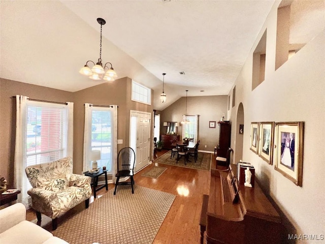 living area with arched walkways, wood finished floors, baseboards, high vaulted ceiling, and an inviting chandelier