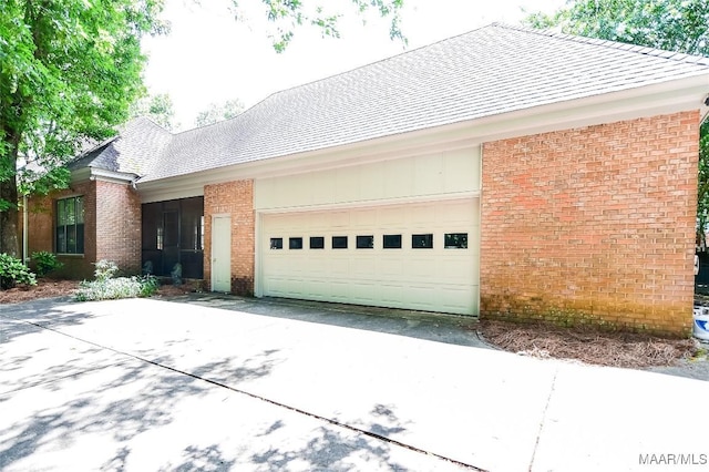 view of home's exterior featuring a shingled roof, an attached garage, driveway, and brick siding