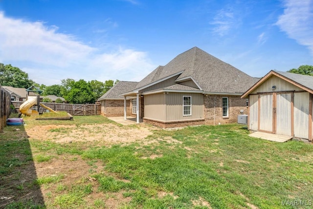 rear view of property featuring a storage shed, a lawn, brick siding, a fenced backyard, and a shingled roof