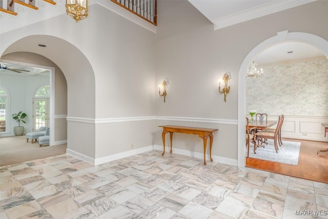 entryway with arched walkways, ceiling fan with notable chandelier, a wainscoted wall, a towering ceiling, and ornamental molding