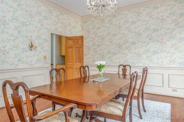 dining room featuring crown molding, wainscoting, light wood-type flooring, and a notable chandelier