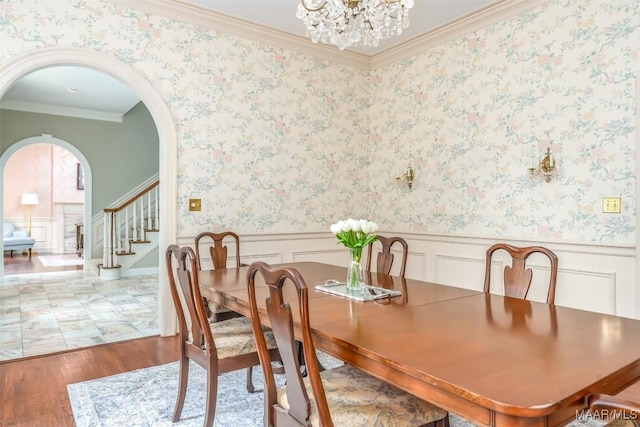 dining room with crown molding, an inviting chandelier, light wood finished floors, a wainscoted wall, and stairs