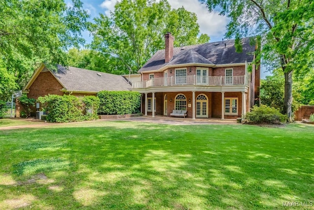 back of house with a yard, brick siding, french doors, and a chimney