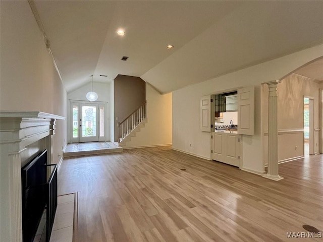 unfurnished living room with ornate columns, light wood finished floors, and a healthy amount of sunlight