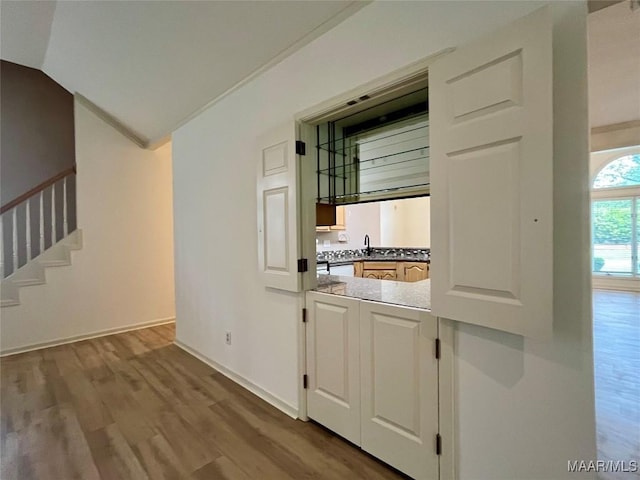 bar with wood finished floors, stairway, baseboards, a sink, and lofted ceiling