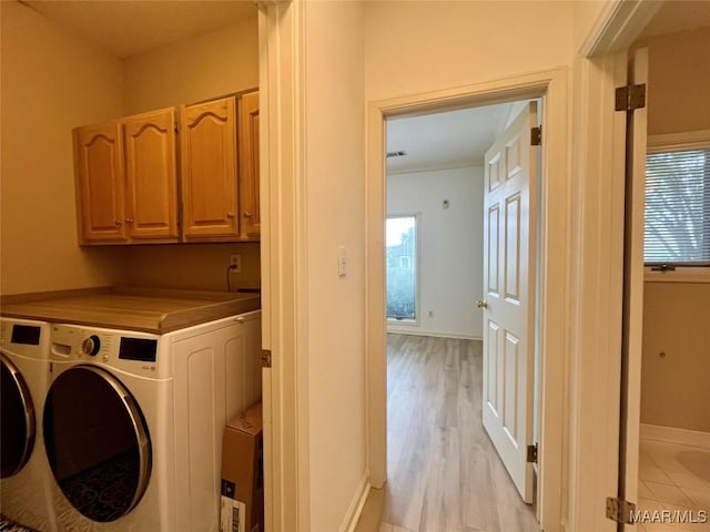 laundry area featuring separate washer and dryer, light wood-style flooring, cabinet space, and plenty of natural light