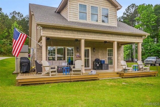 back of property with a lawn, ceiling fan, roof with shingles, and a wooden deck