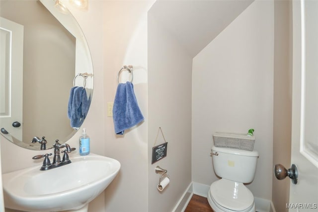 half bathroom with toilet, baseboards, a sink, and lofted ceiling