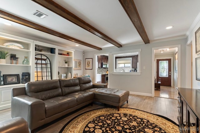 living room featuring light wood-style floors, baseboards, beamed ceiling, visible vents, and ornamental molding
