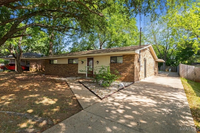 ranch-style house featuring concrete driveway, brick siding, and fence