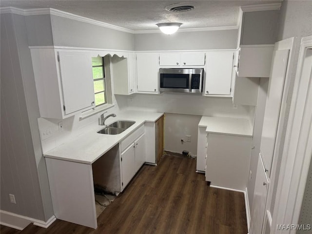 kitchen with a sink, dark wood finished floors, stainless steel microwave, and white cabinets
