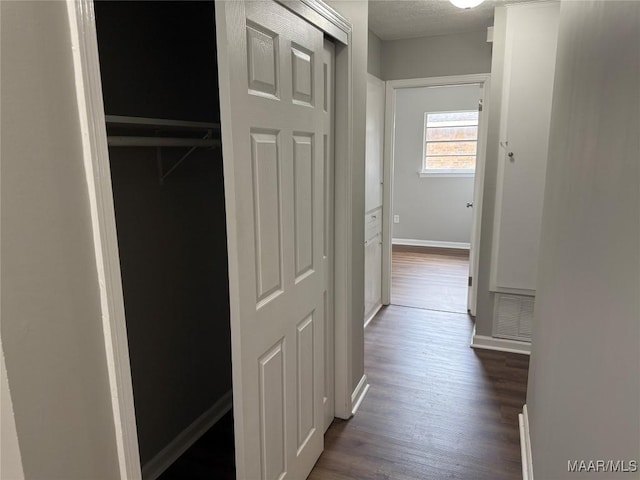 corridor with baseboards, visible vents, a textured ceiling, and dark wood-type flooring