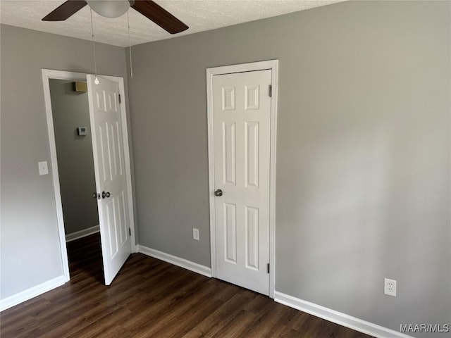 unfurnished bedroom with a textured ceiling, baseboards, dark wood-style floors, and a ceiling fan
