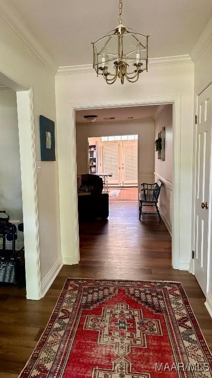 corridor with crown molding, baseboards, an inviting chandelier, and wood finished floors