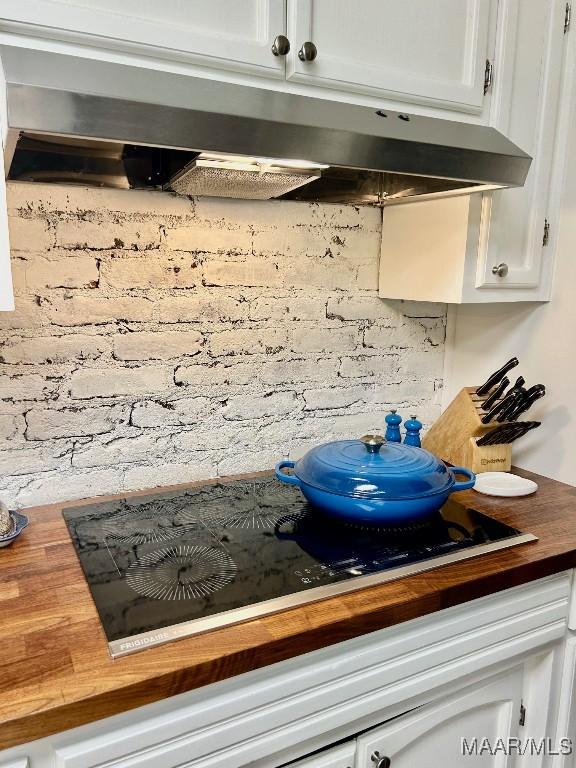 details featuring under cabinet range hood, white cabinets, wooden counters, and black electric stovetop