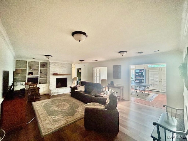 living area featuring a fireplace, a textured ceiling, built in features, wood finished floors, and ornamental molding