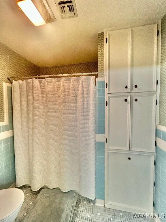 bathroom featuring tile patterned flooring, visible vents, toilet, tile walls, and a shower with curtain