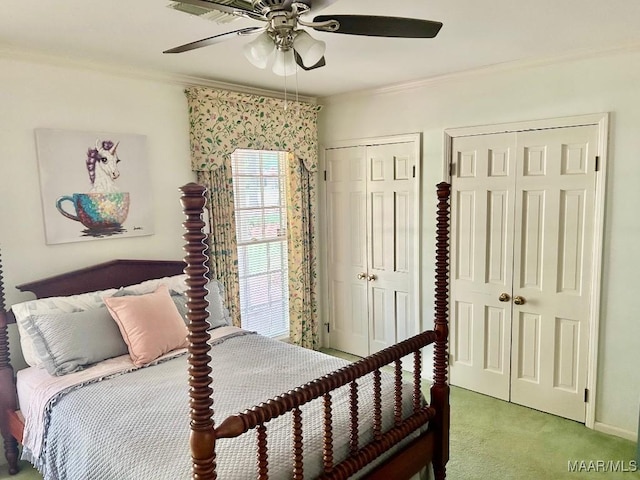bedroom featuring a ceiling fan, ornamental molding, light carpet, and two closets