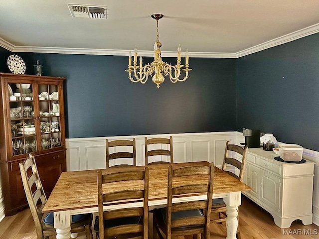 dining space with an inviting chandelier, crown molding, light wood finished floors, and visible vents