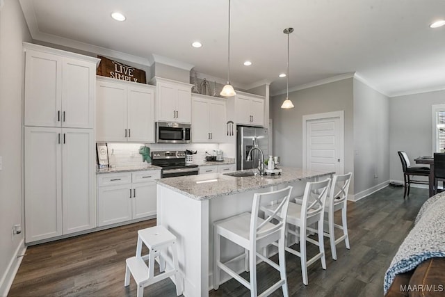 kitchen featuring crown molding, white cabinets, a sink, stainless steel appliances, and a center island with sink
