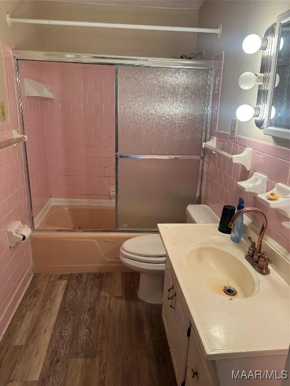 bathroom featuring tile walls, wood finished floors, vanity, toilet, and enclosed tub / shower combo