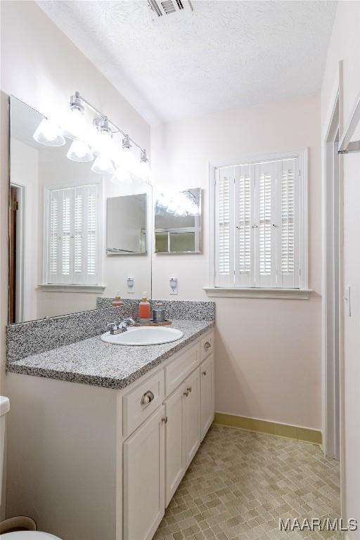 bathroom featuring vanity, a textured ceiling, baseboards, and visible vents