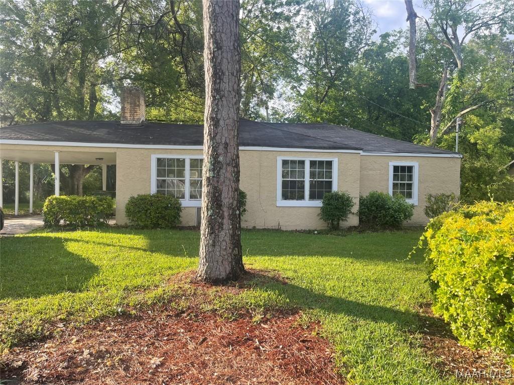 ranch-style home with a carport, stucco siding, a chimney, and a front yard