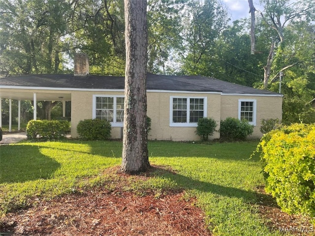 ranch-style home with a carport, stucco siding, a chimney, and a front yard