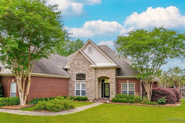 view of front of house featuring stone siding, a front yard, roof with shingles, stucco siding, and a standing seam roof