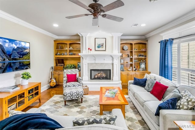 living room with a ceiling fan, visible vents, crown molding, a fireplace, and wood finished floors