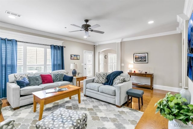 living room featuring ceiling fan, visible vents, arched walkways, light wood-type flooring, and ornamental molding