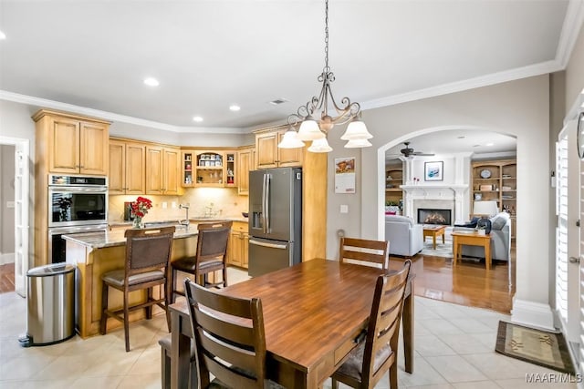dining room featuring a ceiling fan, crown molding, arched walkways, a fireplace, and light tile patterned floors